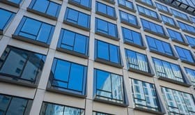 Imagen de edificio con predominio de ventanas en la fachada. Reflejan el color azul del cielo, que baña la imagen.